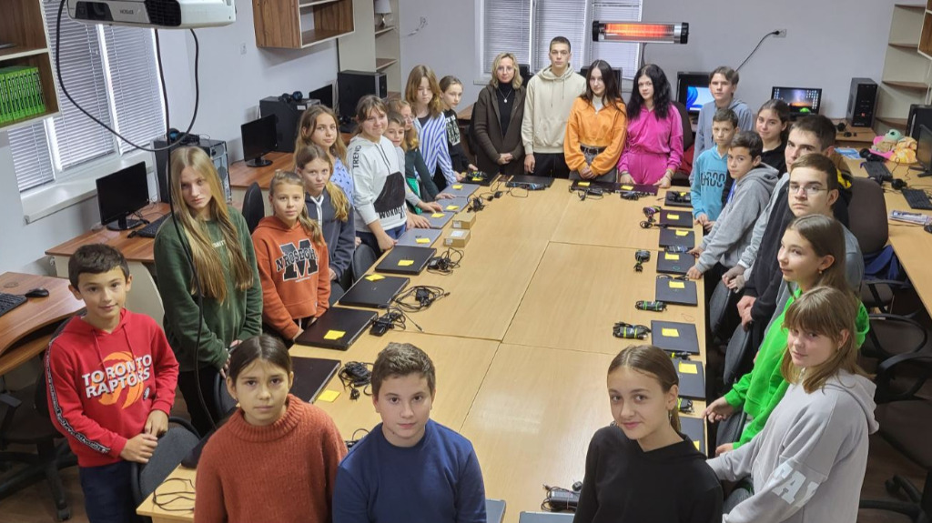 Laptops to Ukraine in 2023 - classroom full of children standing around a long table with laptop computers on it